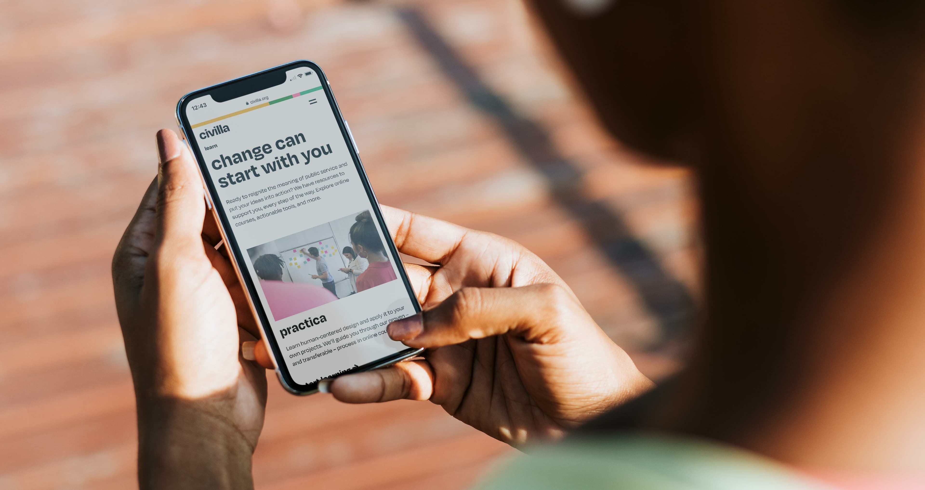 A person holding a smartphone and reading an article titled "Change can start with you" on the screen. The background is blurred, focusing on the phone and the person's hands. The article appears to discuss practice and engagement.