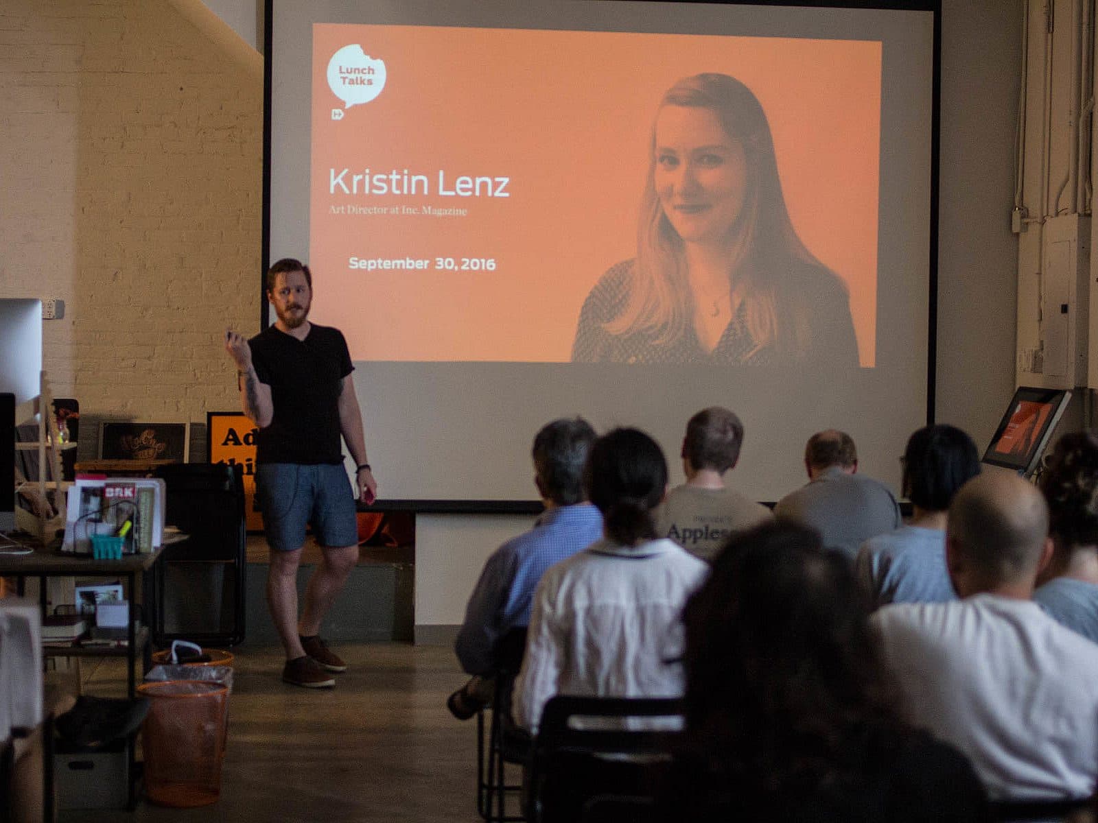 A speaker stands in front of an audience, gesturing with his right hand. A presentation slide behind him shows a woman's photo with the text "Kristin Lenz, Art Director of The Magazine" and the date "September 30, 2016." The audience is seated and attentive.
