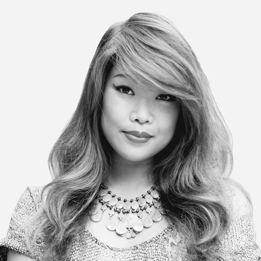 Black and white image of a woman with long, wavy hair styled to the side. She is wearing a textured top and a statement necklace with large, round beads. Her expression is calm and composed, and she is looking directly at the camera.