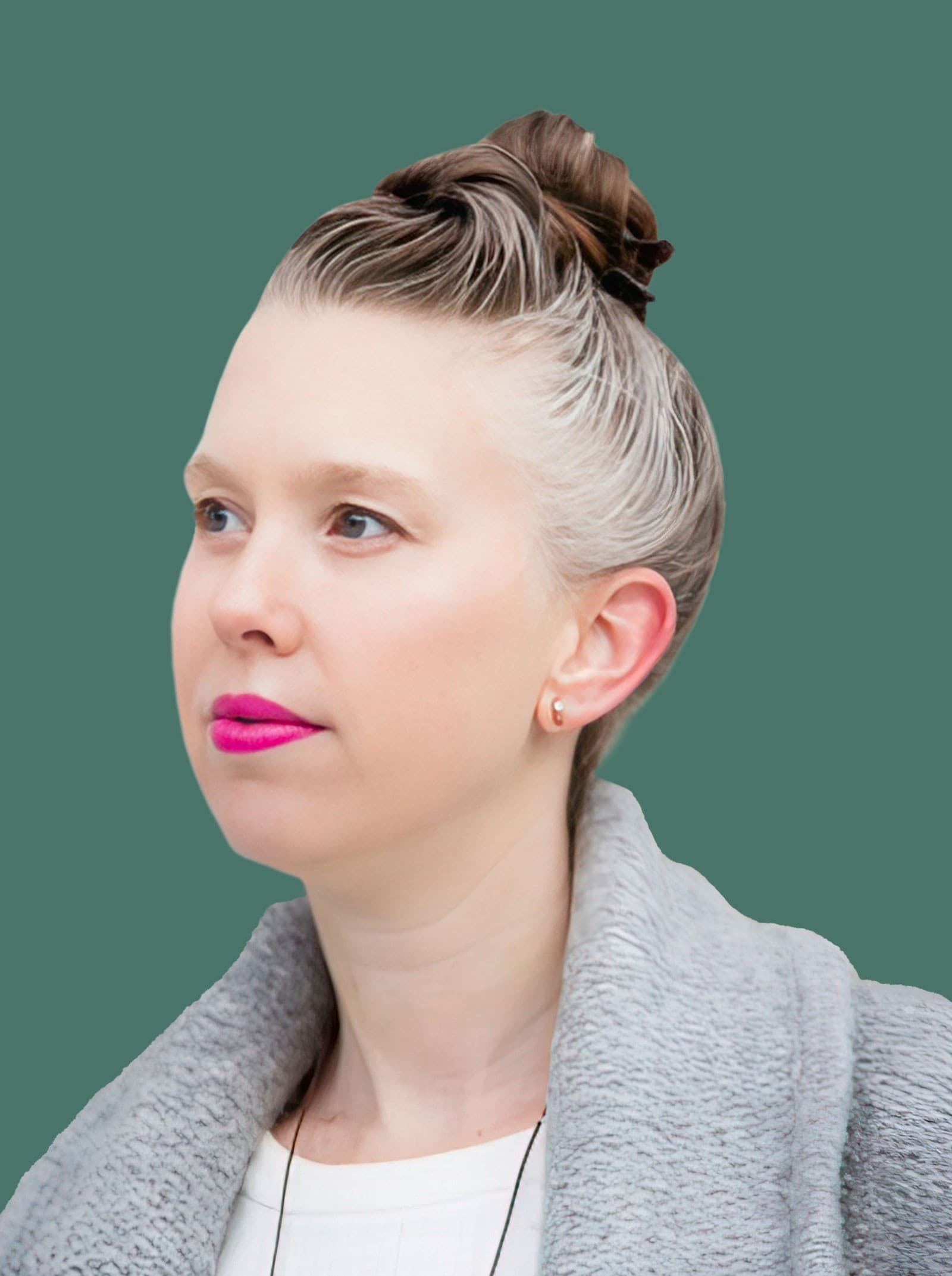 A woman with light skin and bright pink lipstick, wearing a gray textured coat and white top, has her hair in a topknot. She looks slightly to the side against a solid green background.