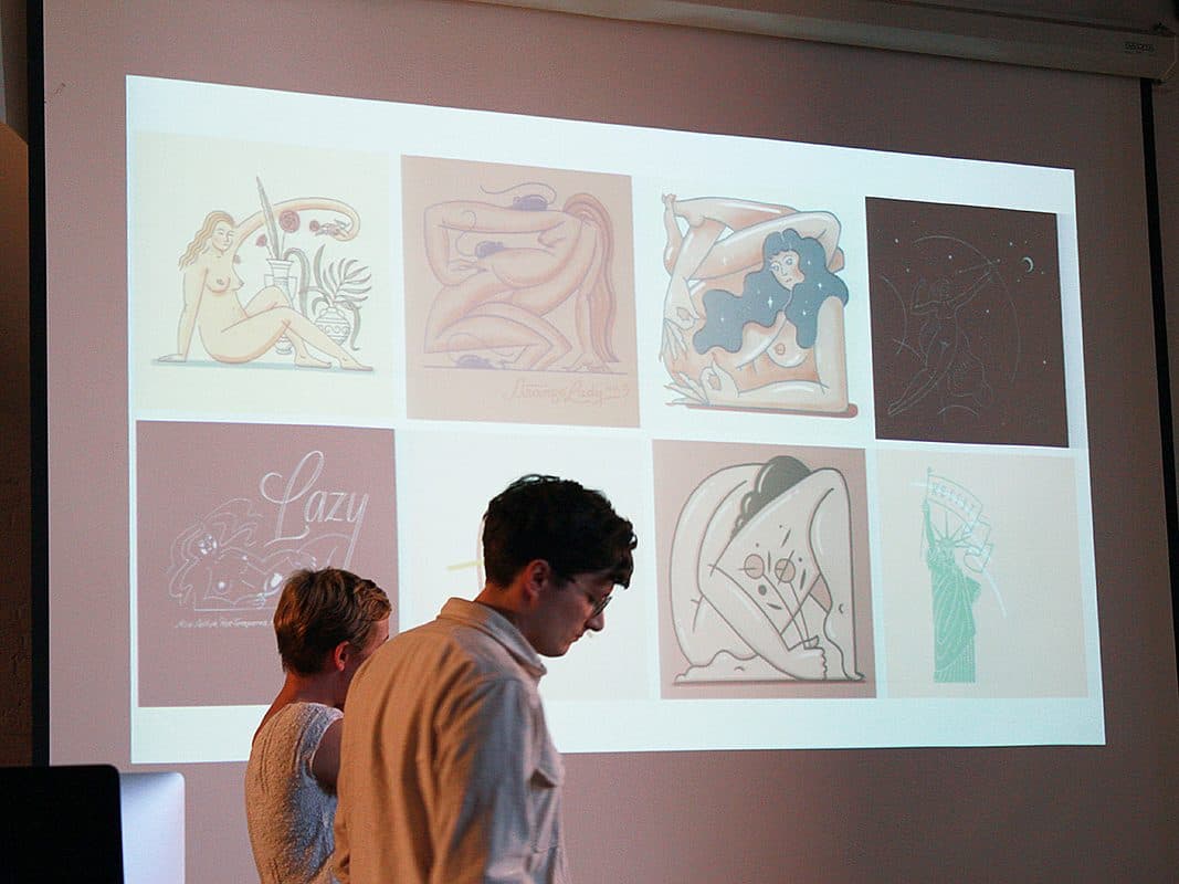 Two individuals stand in front of a projection screen displaying various illustrations. The artworks include abstract figures, a reclining woman, a "lazy" character, and creative depictions. The room appears dimly lit, focusing attention on the projected images.