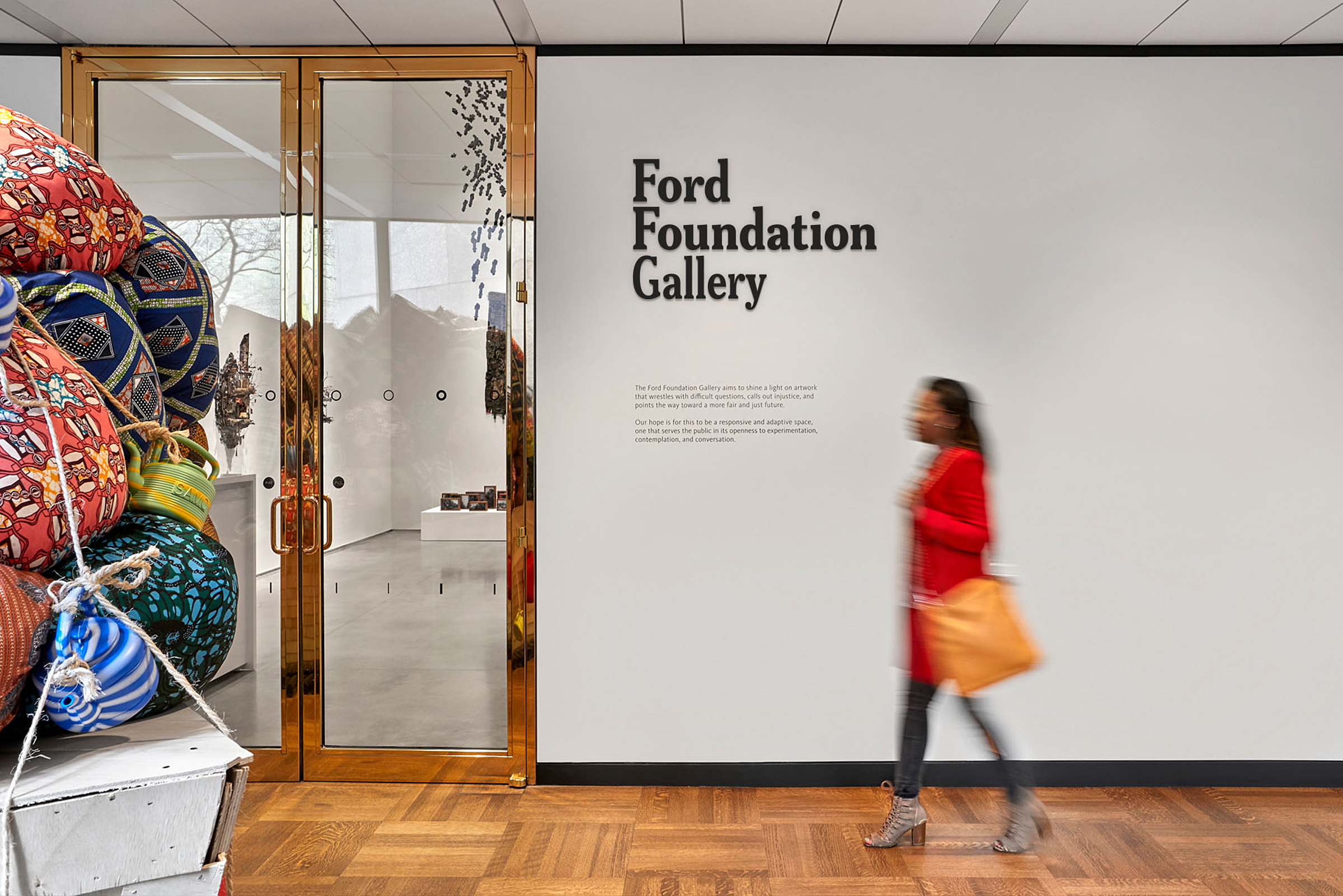 Woman wearing red walking in front of Ford Foundation Gallery signage