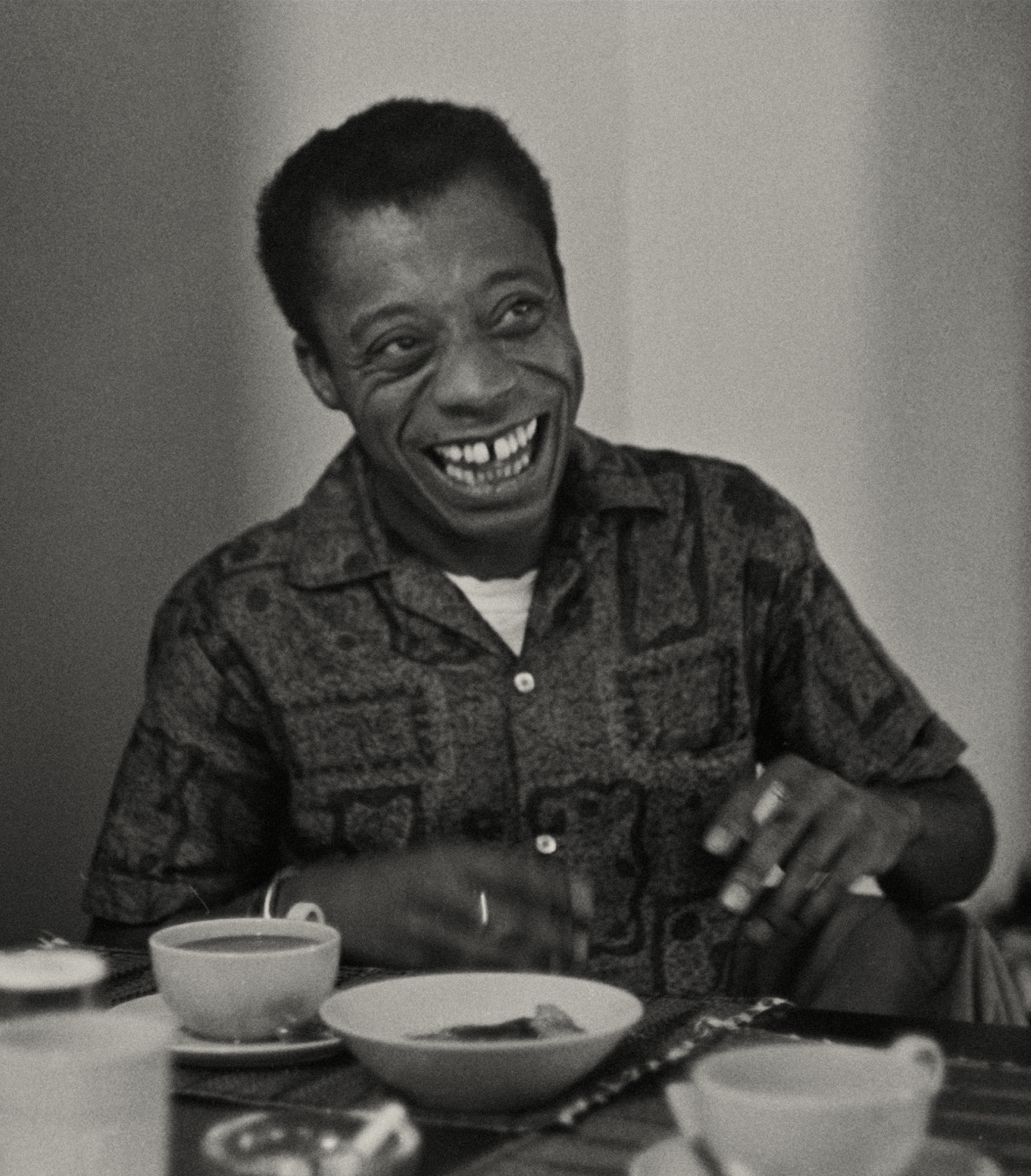 Black and white photo of James Baldwin smiling and drinking tea